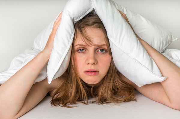 Young woman who has Crohn's and can't sleep covering her head with a pillow