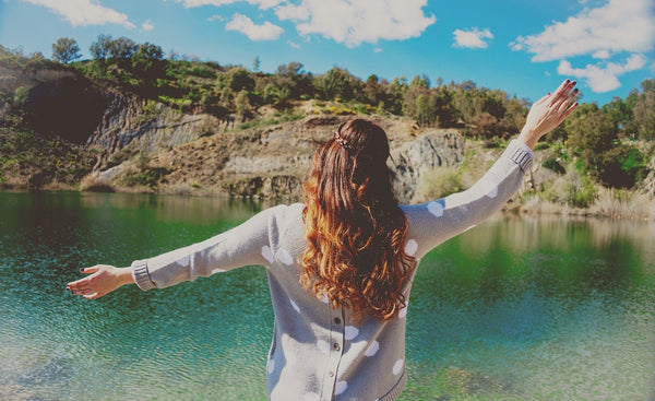 Supplements for inflammation: A happy woman spreads her arms in front of a lake and hill